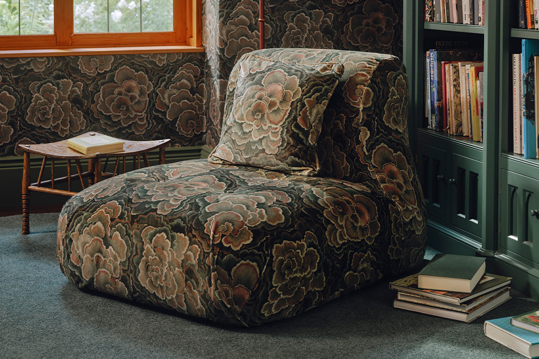 a chair with a floral pattern on the floor next to a bookcase