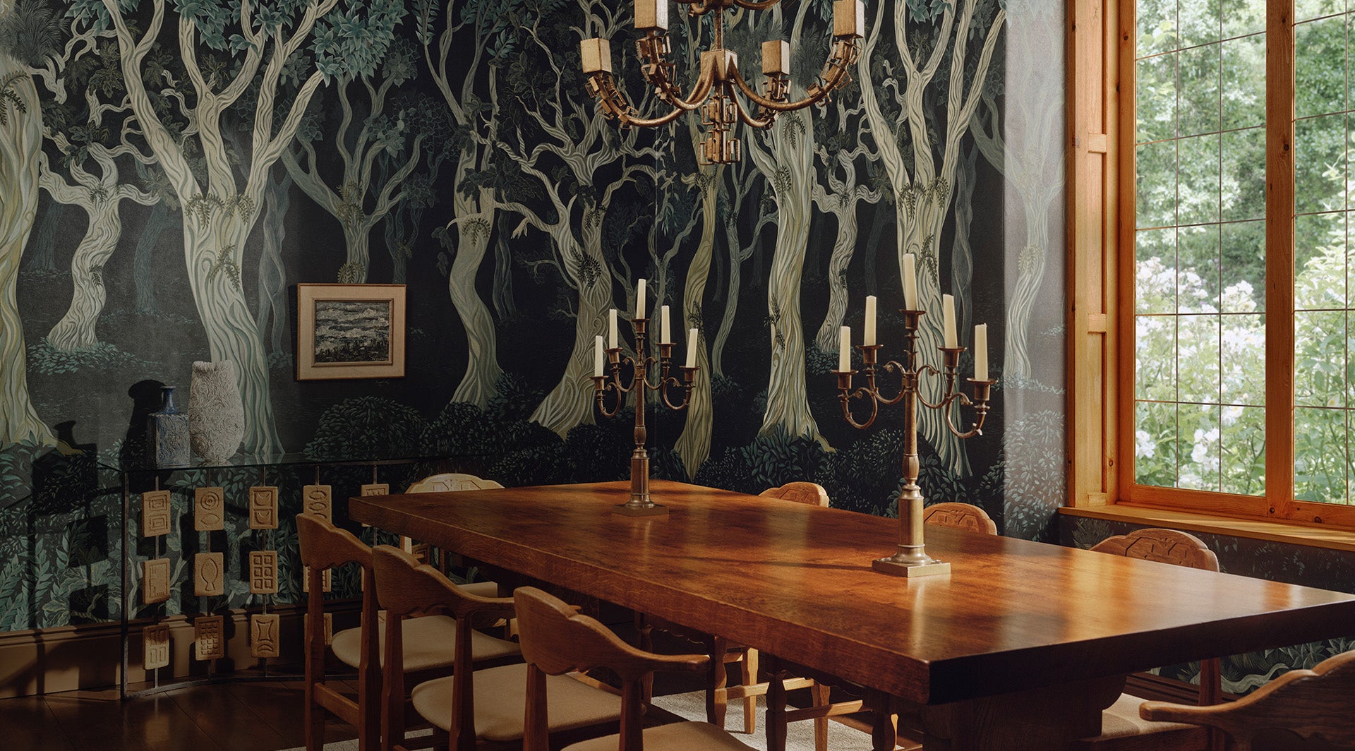 a table with candles on it and a chandelier in front of a wall with trees
